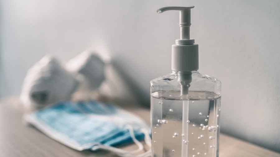 Une bouteille de désinfectant pour les mains à côté d'une pile de masques faciaux.