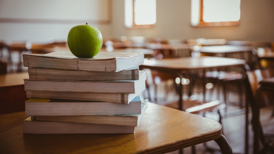 An apple sitting on top of a stack of books in a classroom.