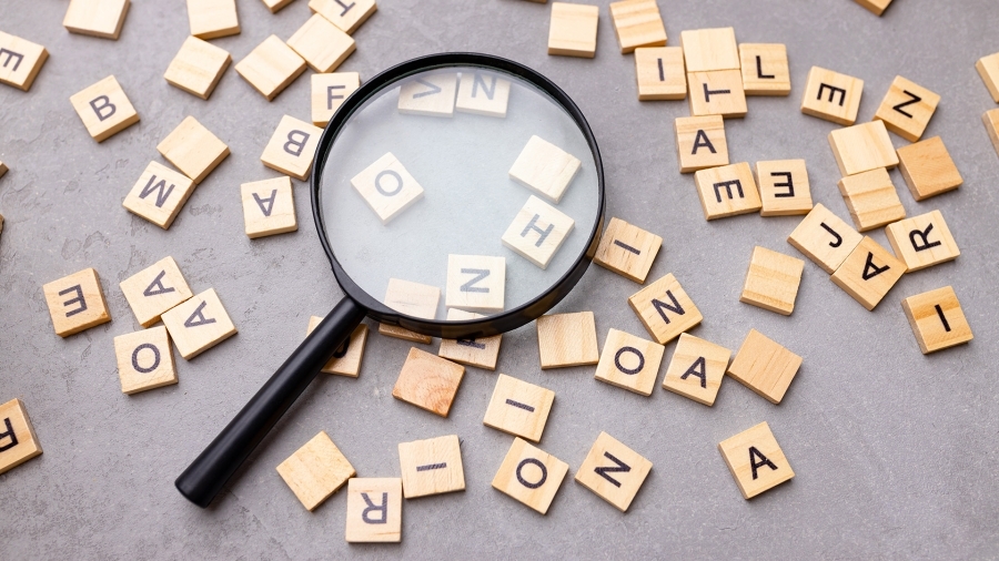 A magnifying class lying among Scrabble letter tiles.