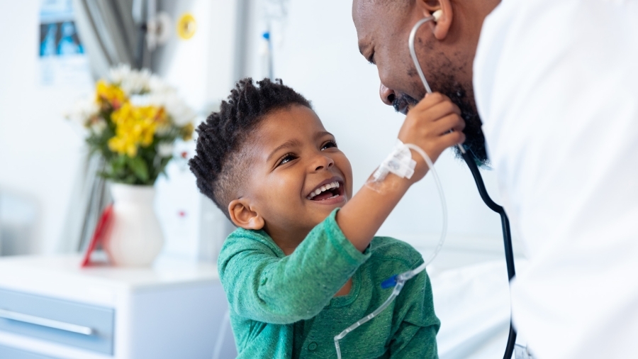 Un enfant souriant et jouant avec le stéthoscope d'un médecin.