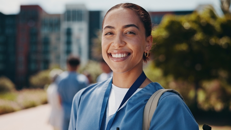 A doctor smiling at the camera, standing in front of a hospital.
