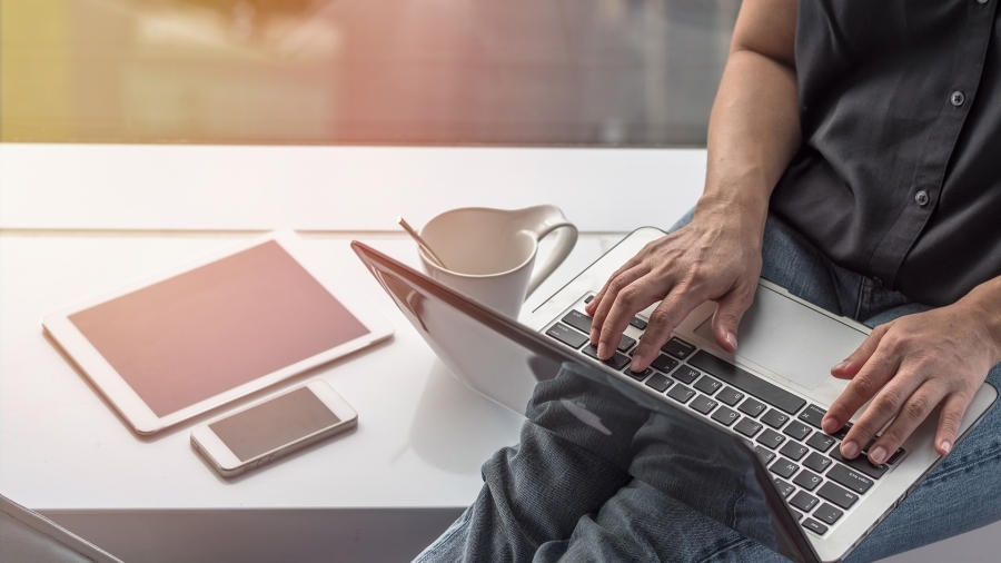 person typing on laptop with mobile devices in front of them, window in the background