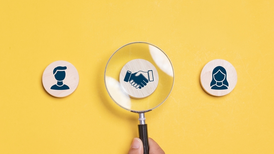 A magnifying glass over an illustration of two people shaking hands.
