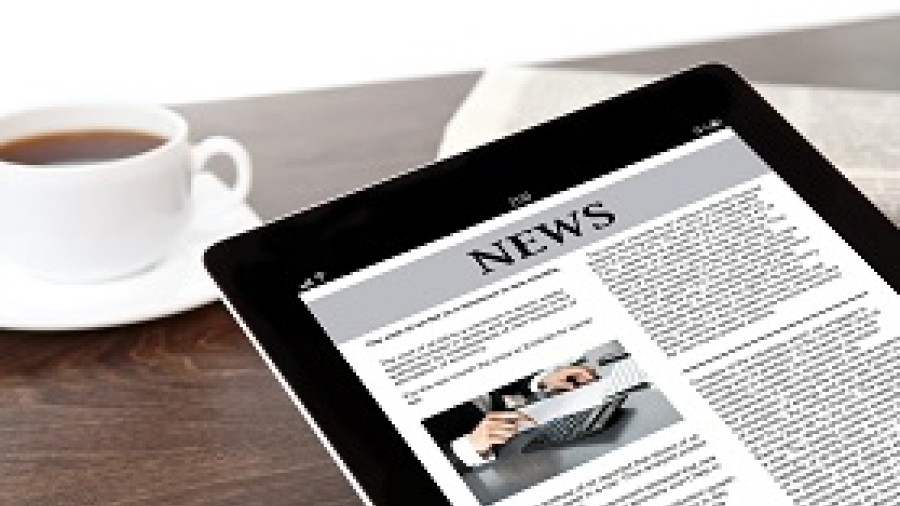 a tablet displaying a news page with a cup of coffee on a table in the background
