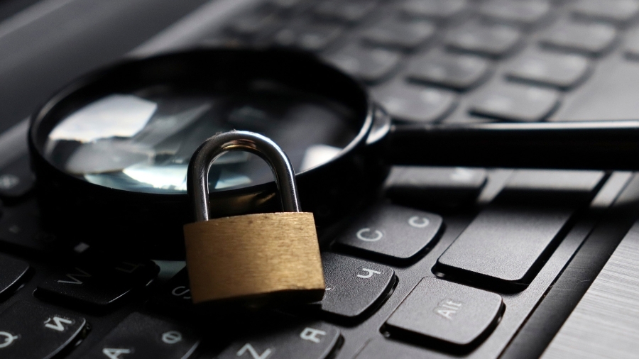 A magnifying glass and a lock sitting on top of a computer keyboard.