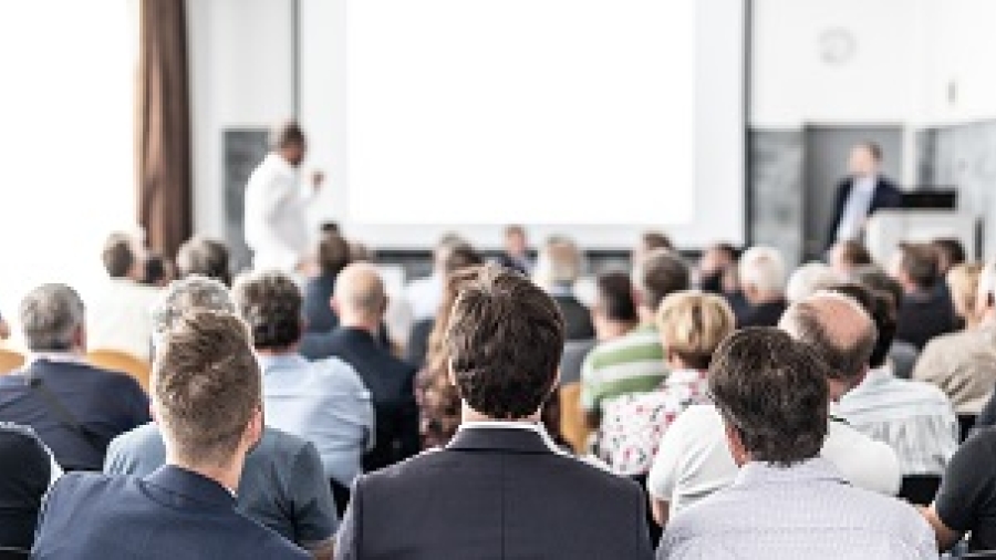 a view from the back of a room showing seated people in businss attire watching a person speak