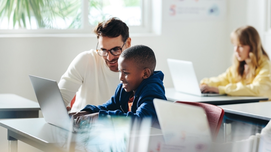 A teacher helps a student using a laptop.