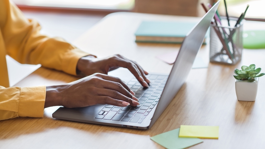 Somebody wearing a yellow sweater typing on a laptop.