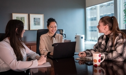 Three IPC staff members sitting at a desk, laughing together.